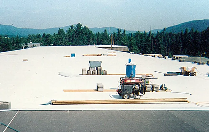 Large white membrane roof nearing completion with the Adirondack foothills behind it