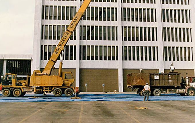 Crane and roll-off container staged beside a multi-story office building for a commercial re-roof