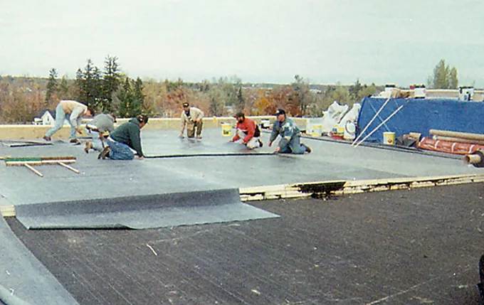 Six-person crew rolling out and seaming a membrane roof on a low-slope building