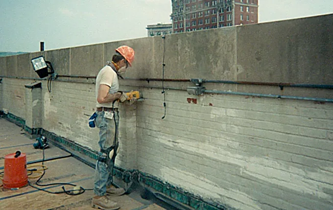 Gates mechanic in a hard hat preparing a masonry parapet wall for waterproofing