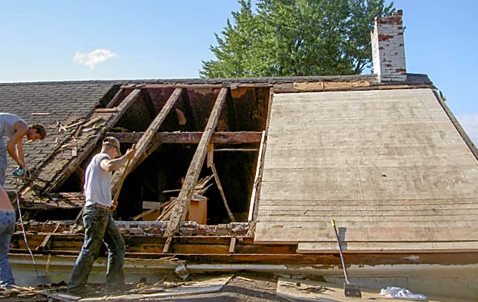 Crew rebuilding rafters and installing new board sheathing on an older home
