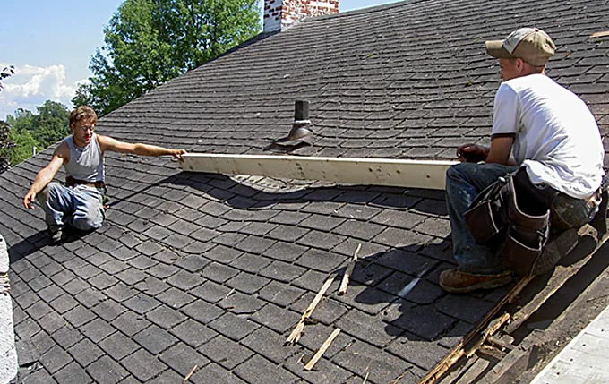 Two Gates Roofing carpenters measuring and fitting new lumber on an asphalt shingle roof