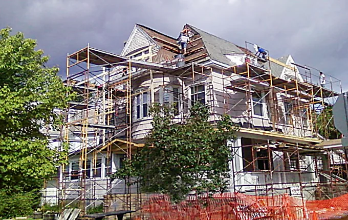Gates Roofing crew on full scaffolding re-roofing a three-story Victorian home under a stormy sky